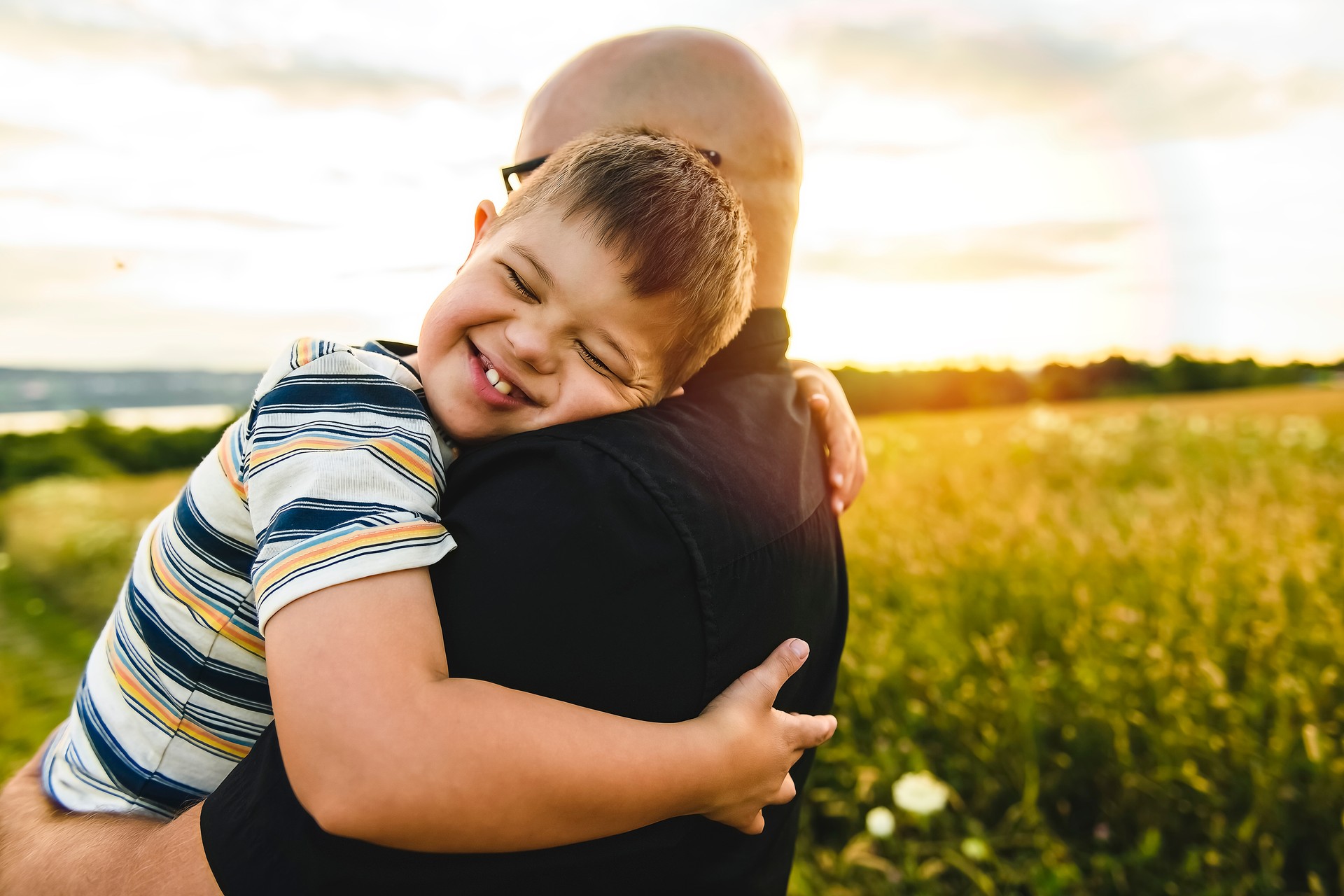 Portrait of a little boy with down syndrome in sunset on summer season with his father