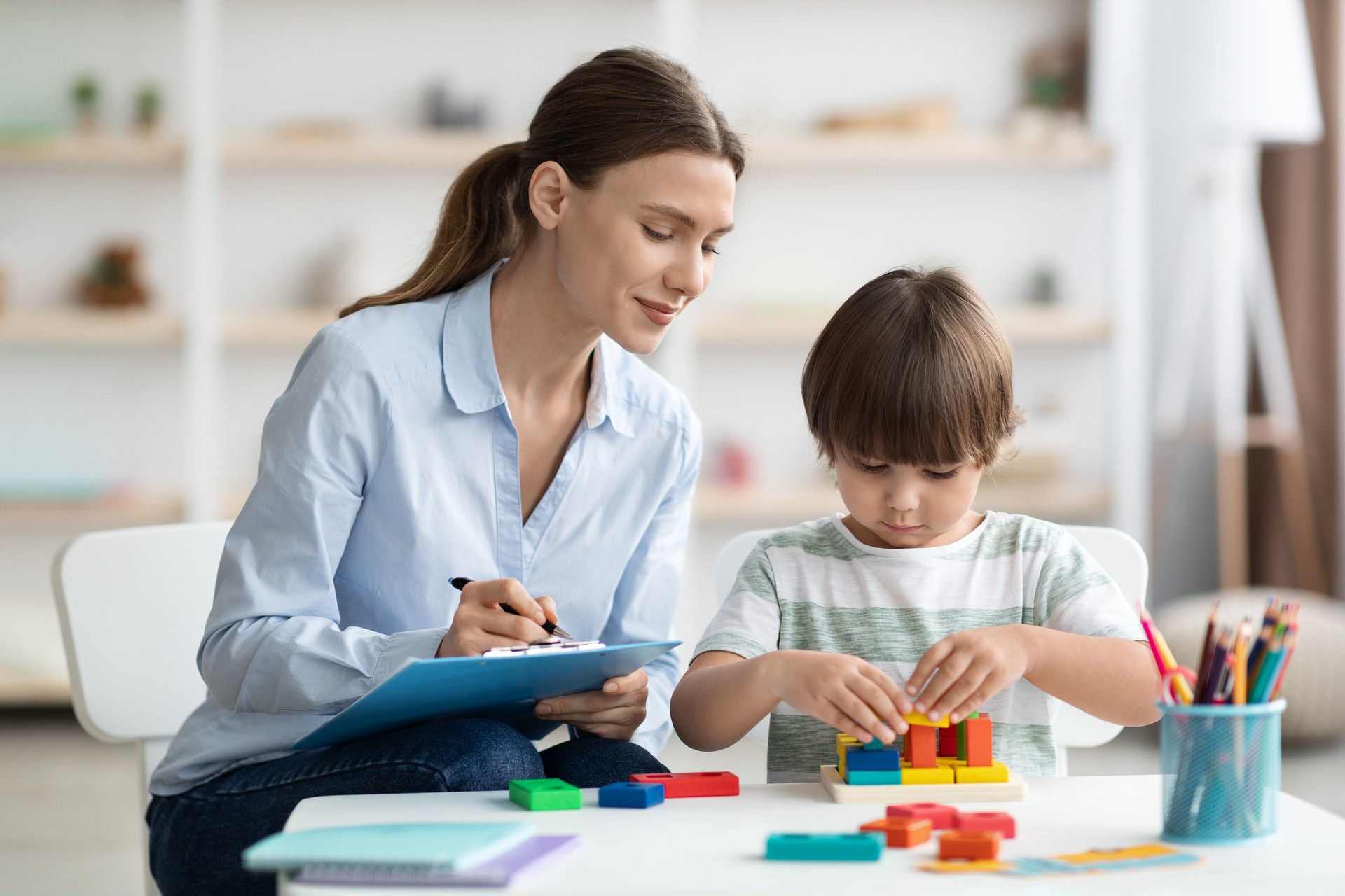 Assessment of kids mental development. Professional woman psychologist watching little boy playing with logical game